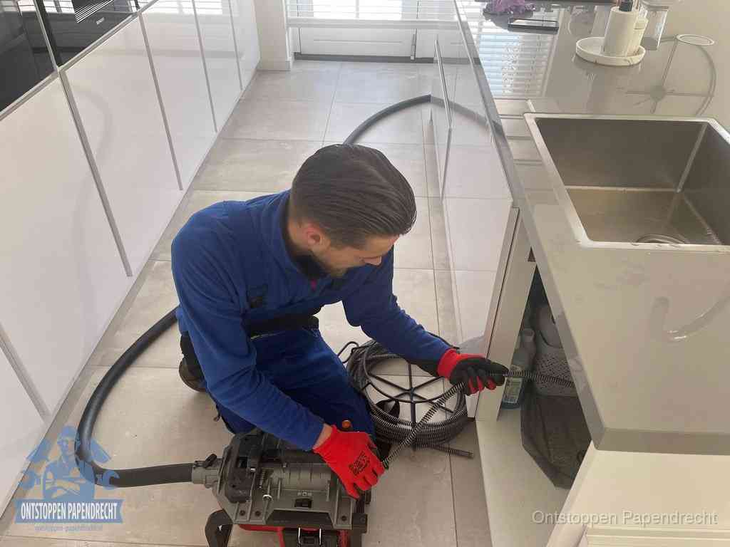 Een monteur ontstopt de keukenafvoer onder de spoelbak met een elektrische veermachine in Papendrecht
