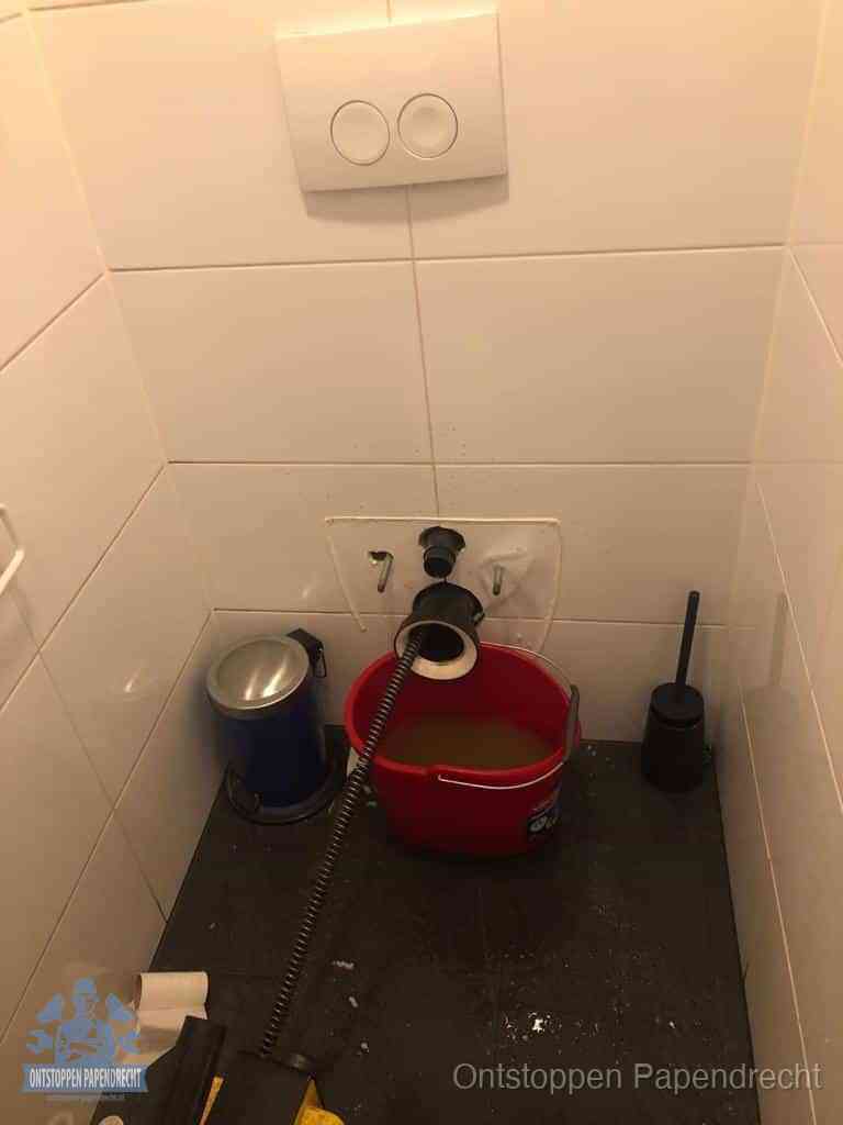 Een ontstopte wand-wc met verwijderde toiletpot waar een ontstoppingsveer in de wanduitgang verdwijnt, het achterhalen waar de verstopping zit in Papendrecht