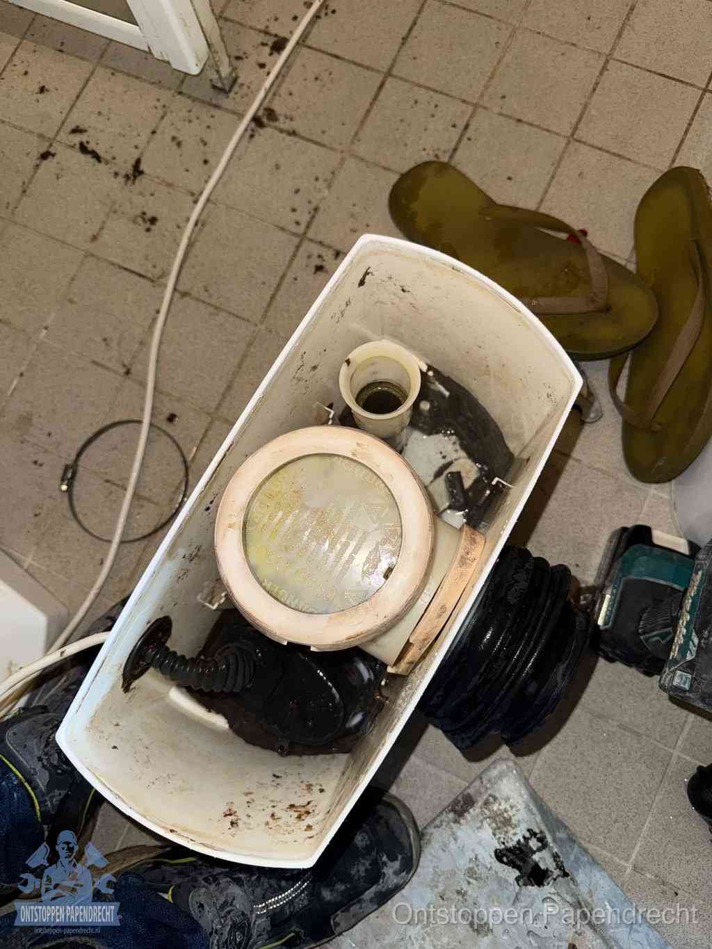 Een gedemonteerde toiletpot op de vloer met ontstoppingsveer en gereedschap ernaast, het verwijderen van een vastzittend voorwerp uit de wc in Papendrecht