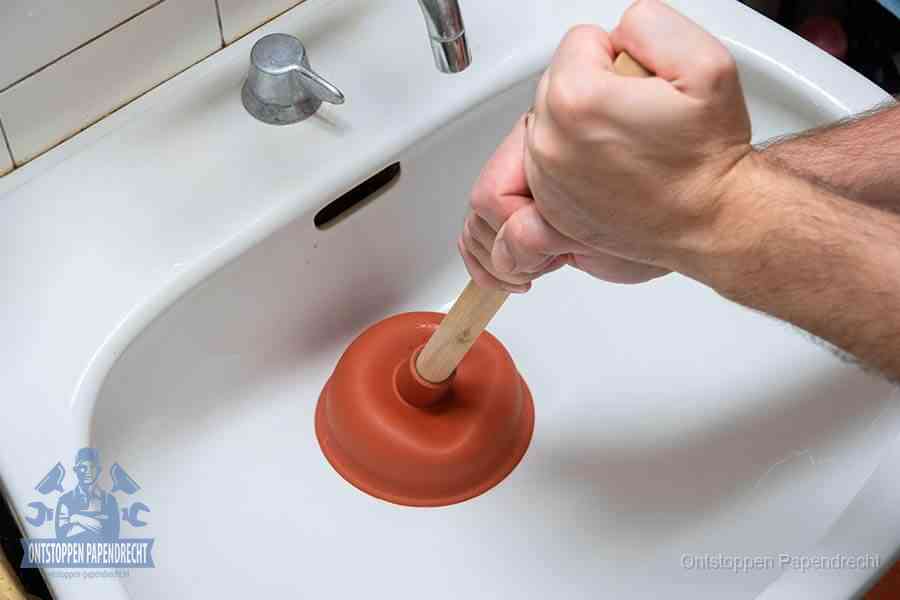 Twee handen gebruiken een rode rubberen plopper op een sanitair-afvoer om het toilet te ontstoppen in Papendrecht