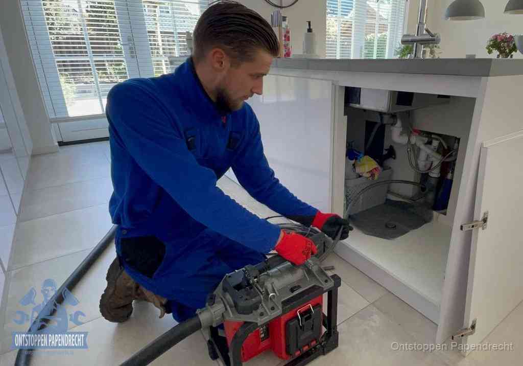 Een monteur voert een professionele elektrische ontstoppingsmachine in de afvoer onder de spoelbak tijdens het gootsteen ontstoppen in Papendrecht